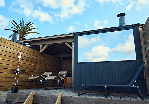 海辺のデッキに建つビーチサウナ小屋とデッキチェア